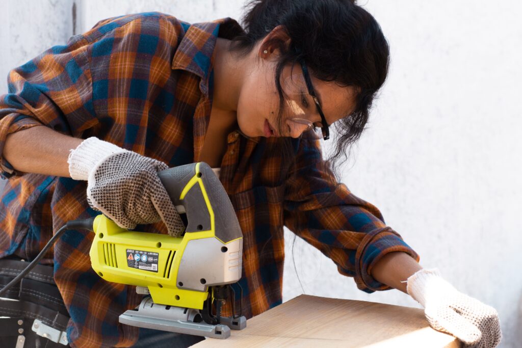 A focused woman uses an electric jigsaw on a wood piece, embodying DIY craftsmanship.